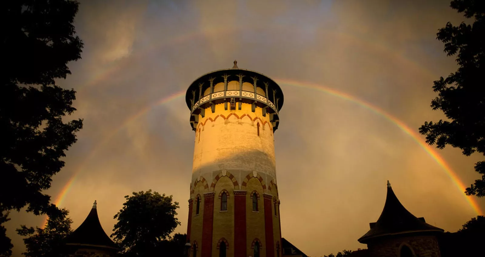 double rainbow over water tower painted red and yellow with pointed top