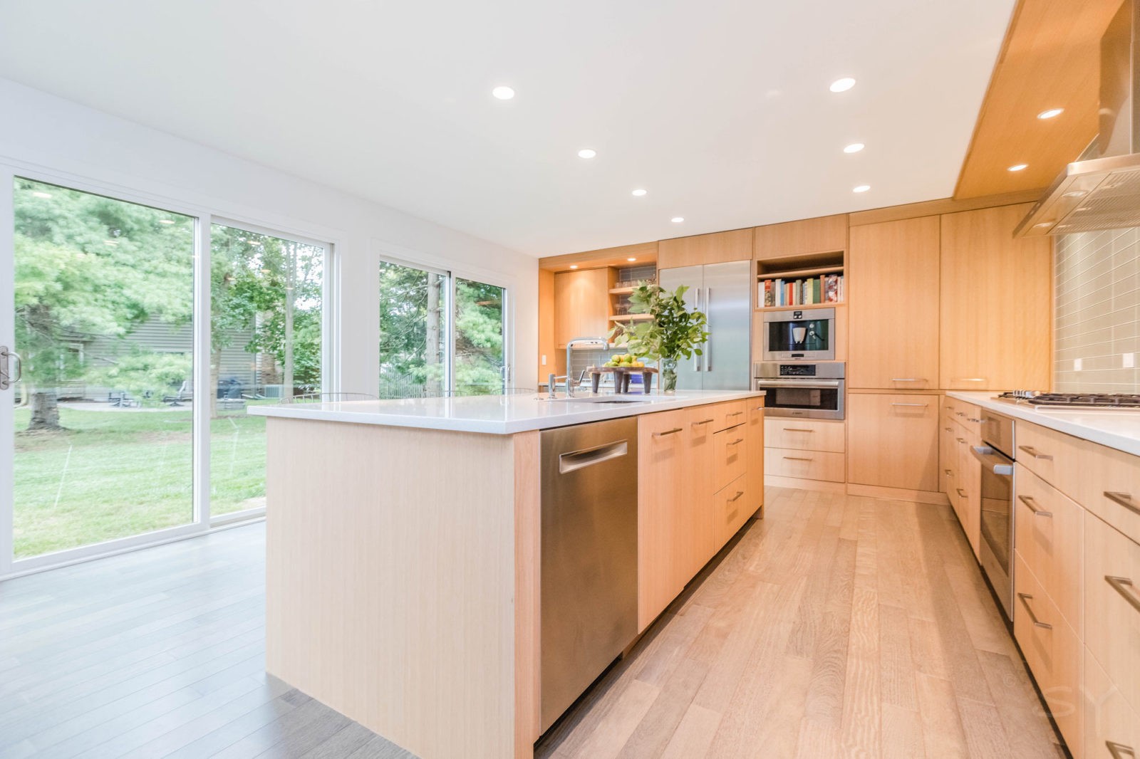 kitchen with large windows light wood cabinets & flooring white island & stainless steel appliances