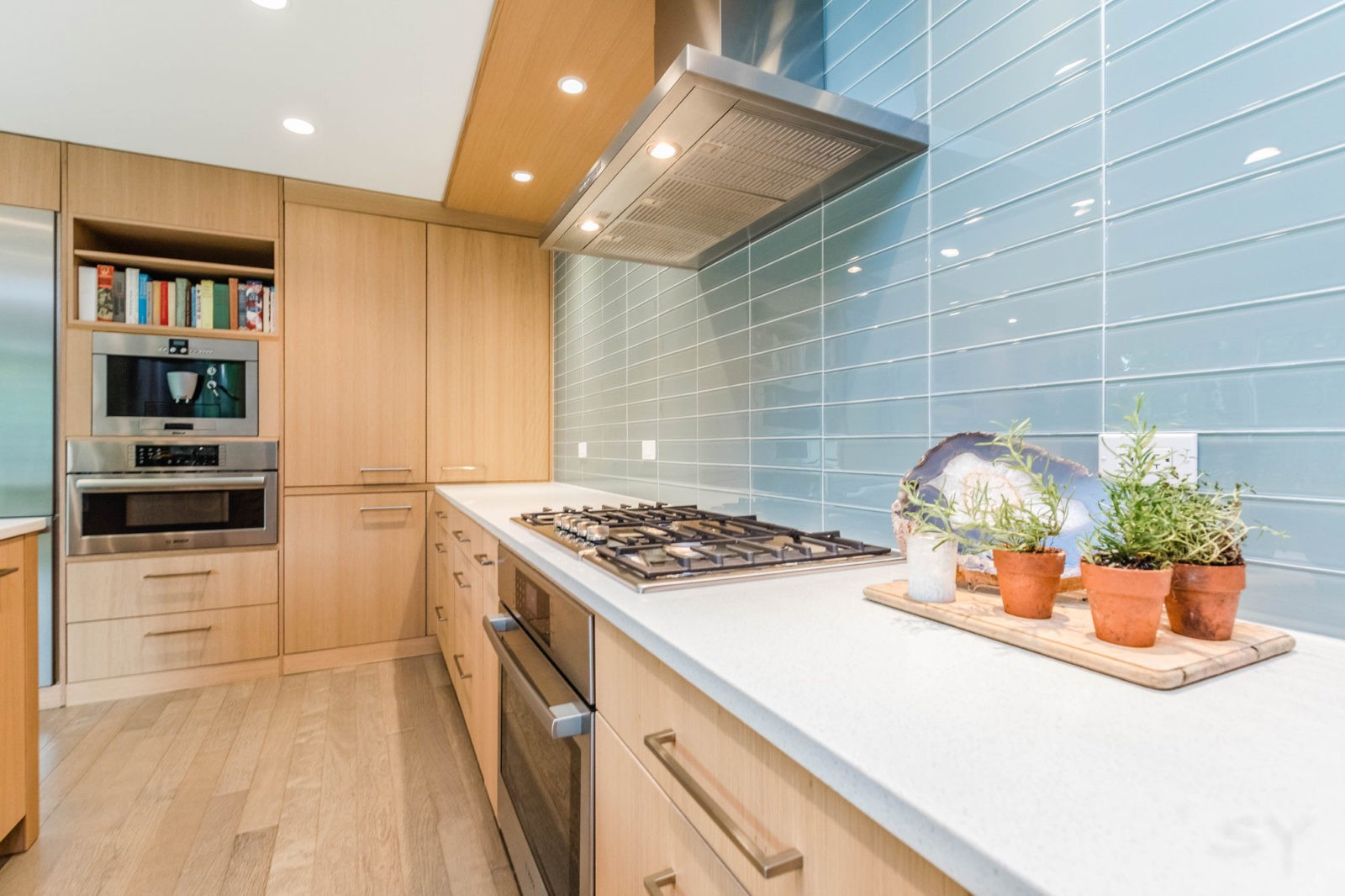Kitchen with island, light wood cabinets & drawers, silver appliances, & light blue tile backsplash