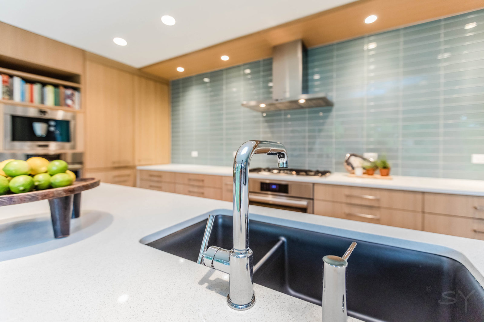 Close-up of stainless steel faucet in updated Brigham kitchen with simplistic light wood cabinets & green/blue subway-tiled backsplash