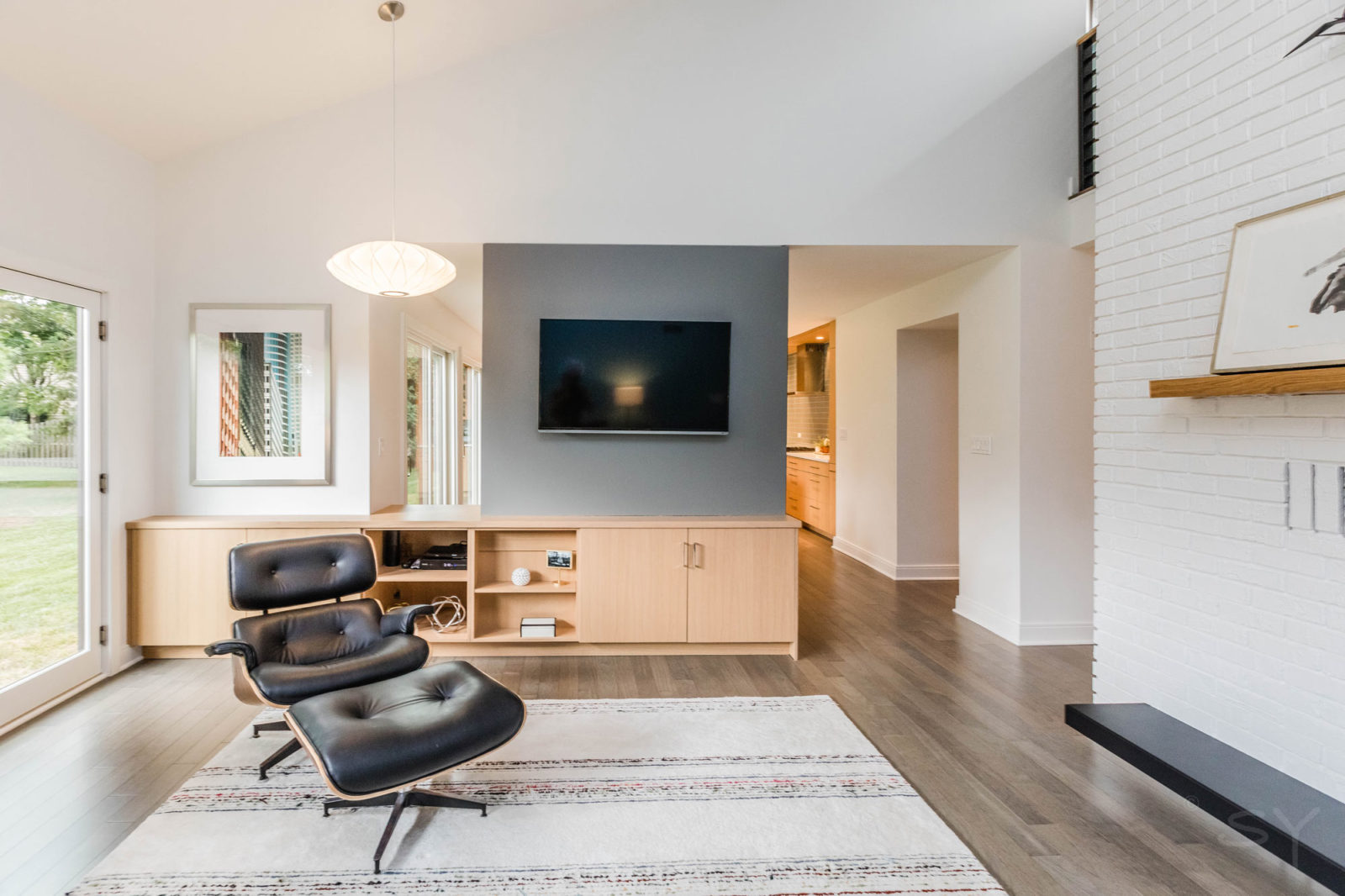 Living room with wall-mounted TV, armchair & ottoman, high ceiling & exterior glass door