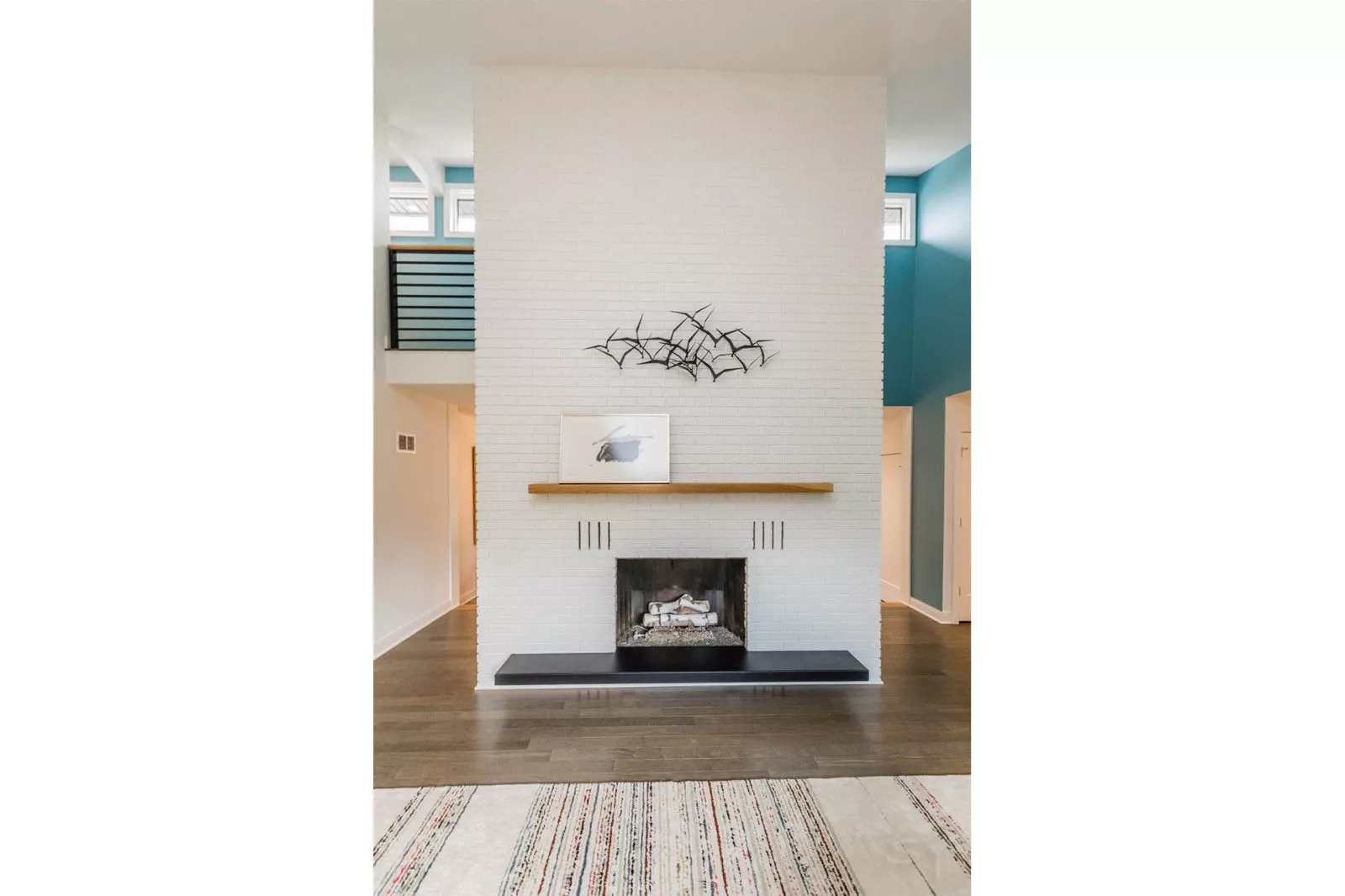 Floor to Ceiling fireplace of white brick a light brown mantle and black base with hardwood floors