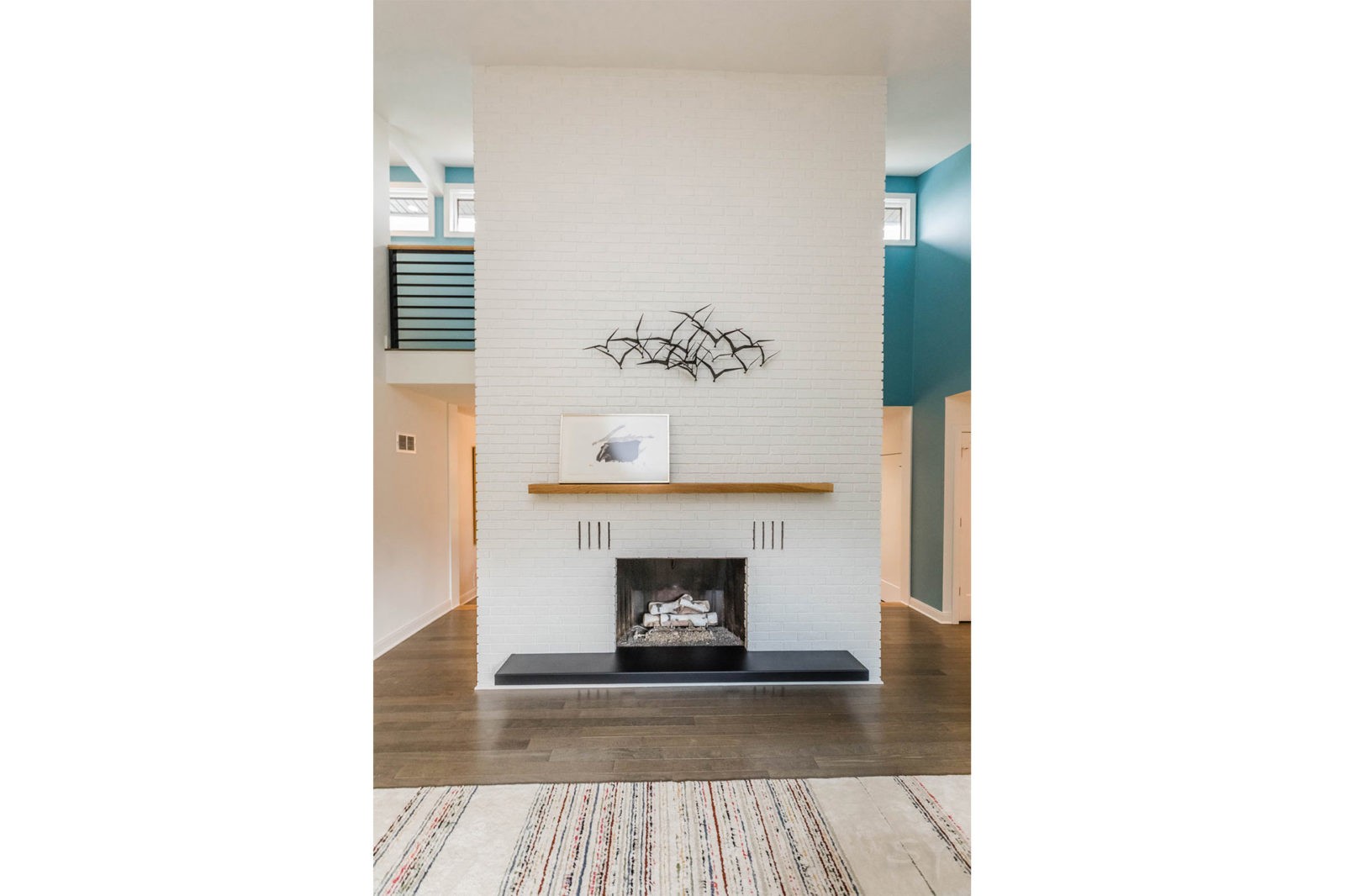 Floor to Ceiling fireplace of white brick a light brown mantle and black base with hardwood floors