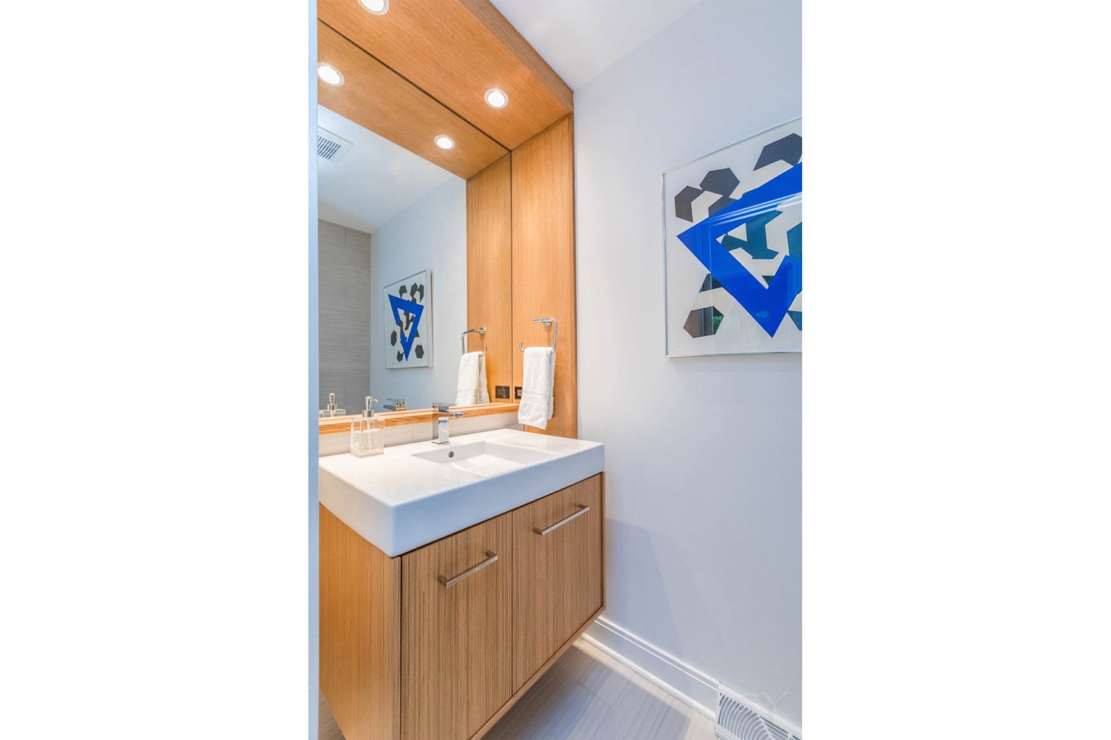 Updated bathroom vanity wrapped in light wood with white marble countertop & royal blue geometric accent art
