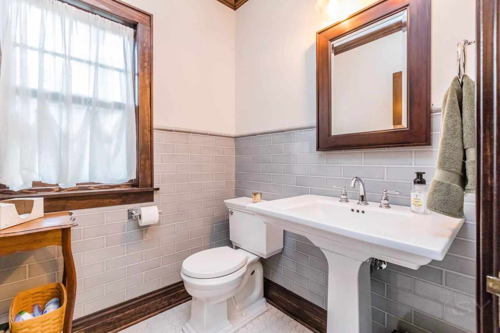 Bathroom with white toilet & sink, bathroom mirror, window, and grey tiled walls