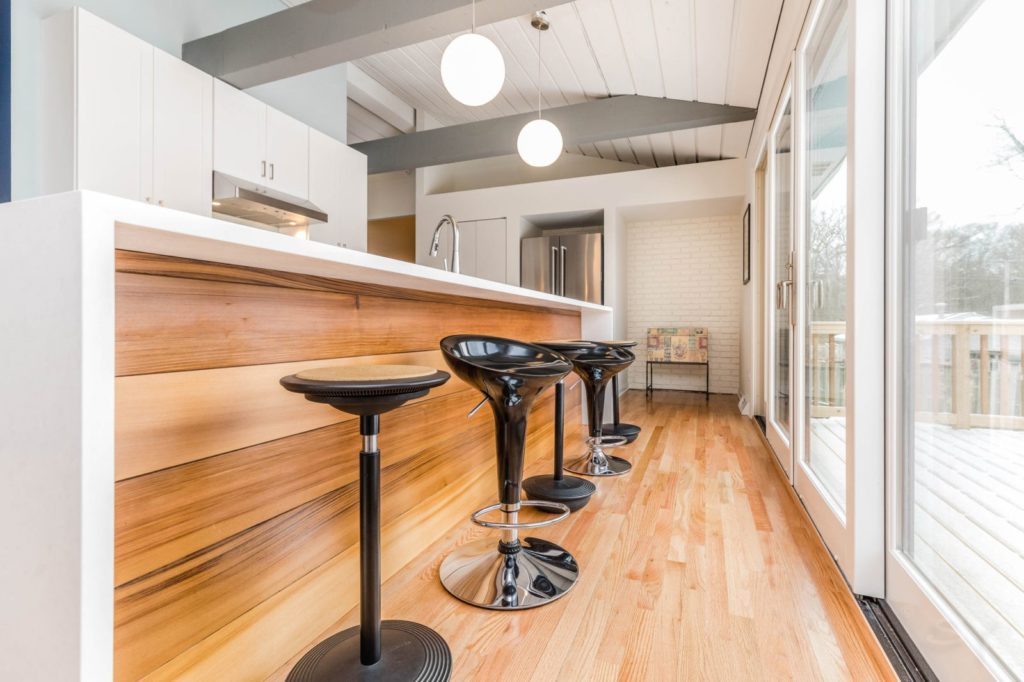 white waterfall countertops on large island in kitchen with black bar stools on light hardwood floor
