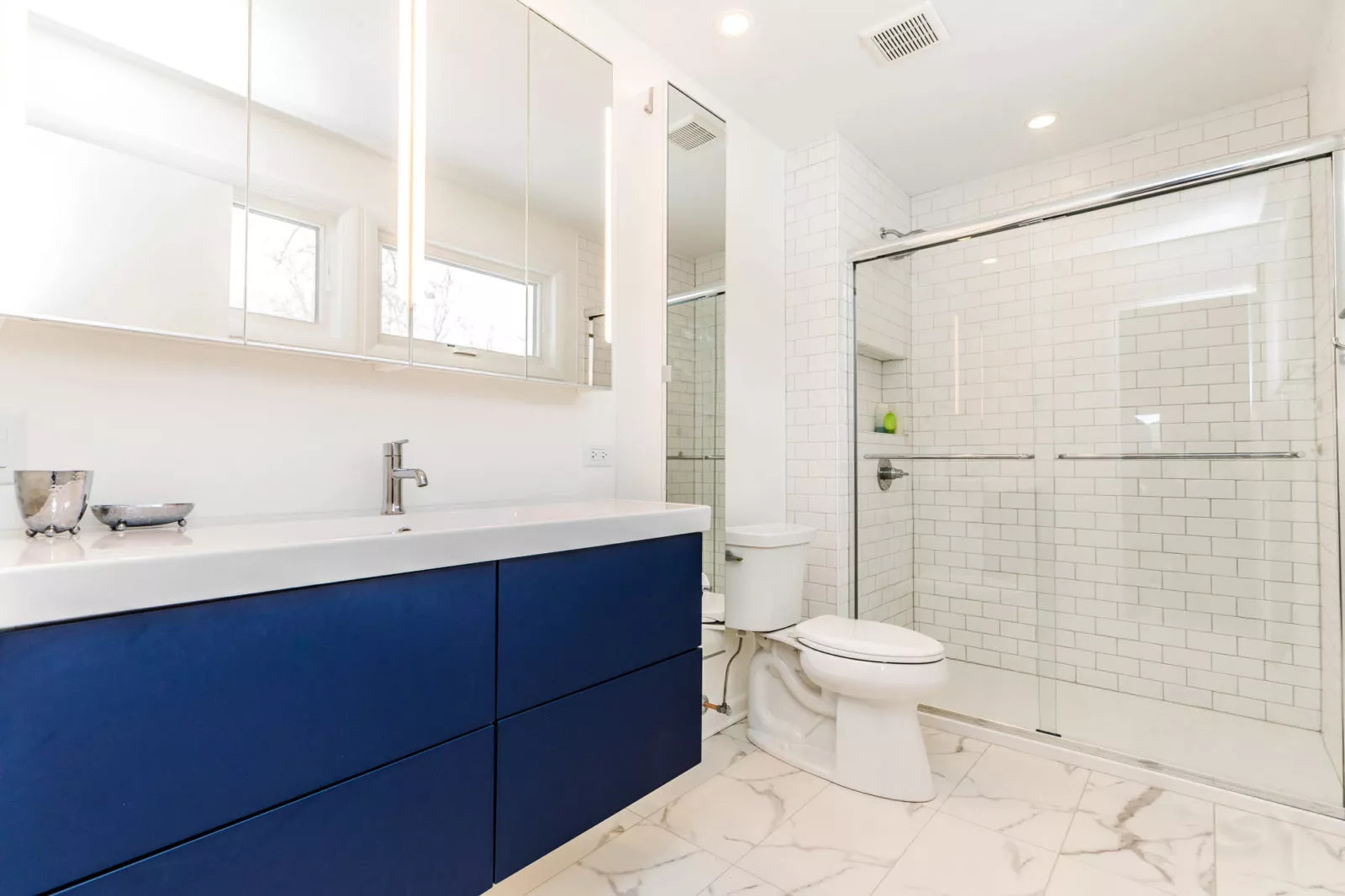 bathroom renovation blue cabinetry glass shower marble flooring subway tile mirror cabinetry