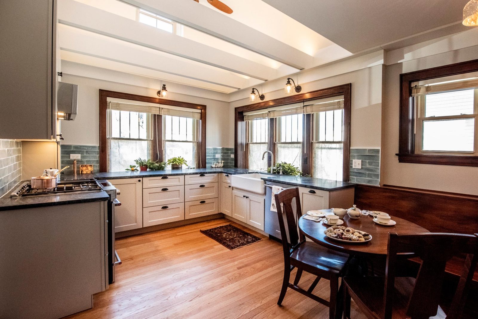 Updated kitchen space with contrasting white cabinets, dark grey marble countertops, green subway tile backsplash, & stained wood windows