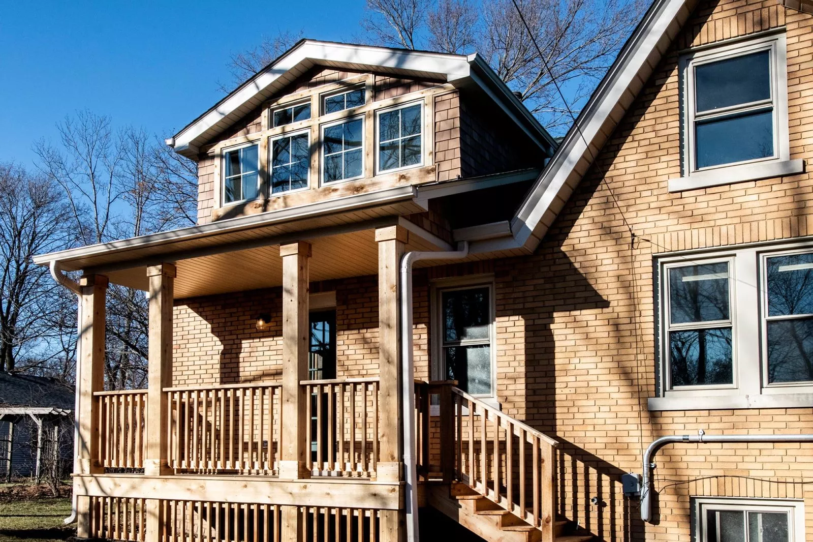 Exterior view of home with second-story cedar shake dormer, matching porch columns, railings, & light brown brick