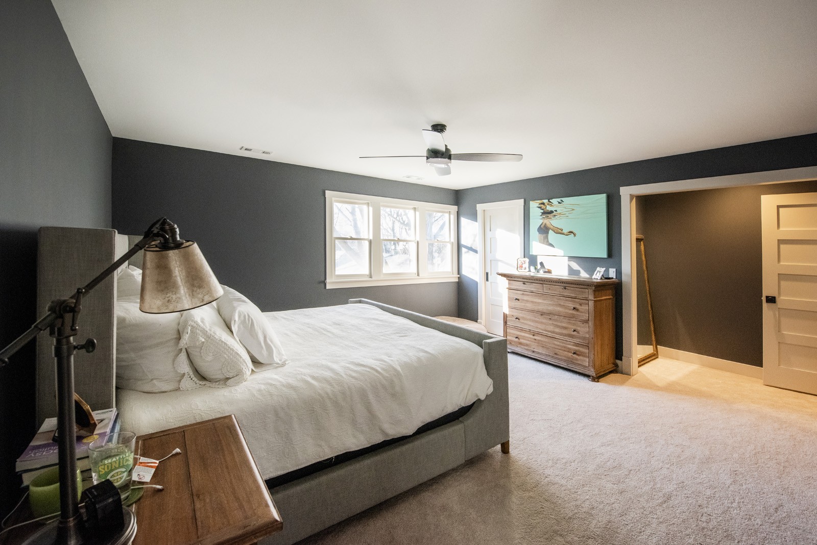 Bedroom with grey walls carpet a grey bed with white bedding and wooden nightstand and dresser