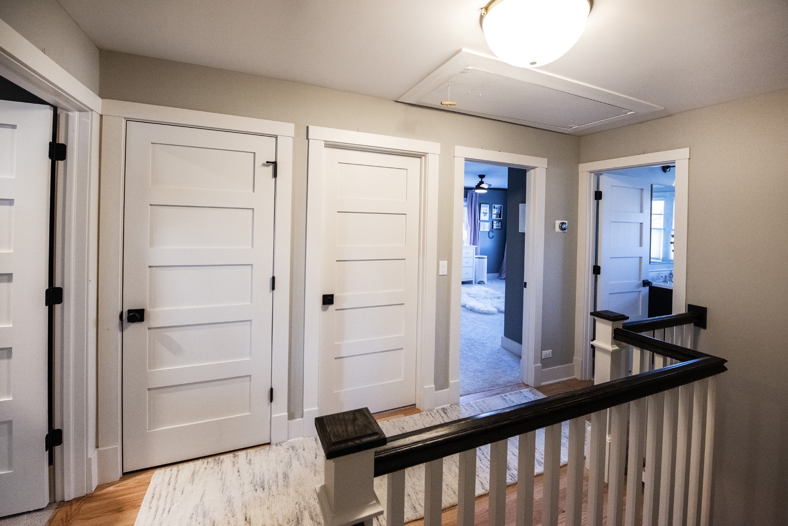 The hallway of the second level of a home with white doors to rooms and a rug on hardwood floors