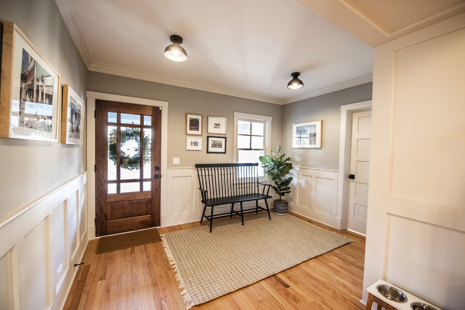 Interior of entry room with black bench, wood floors, grey walls with picture frames, pet bowls