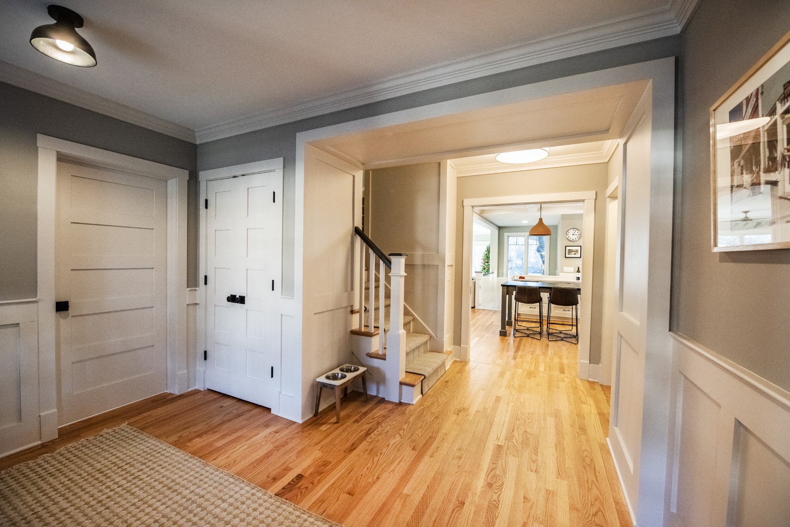 Long view of updated entryway leading into kitchen with grey walls, white crown moulding, & custom white-paneled doors