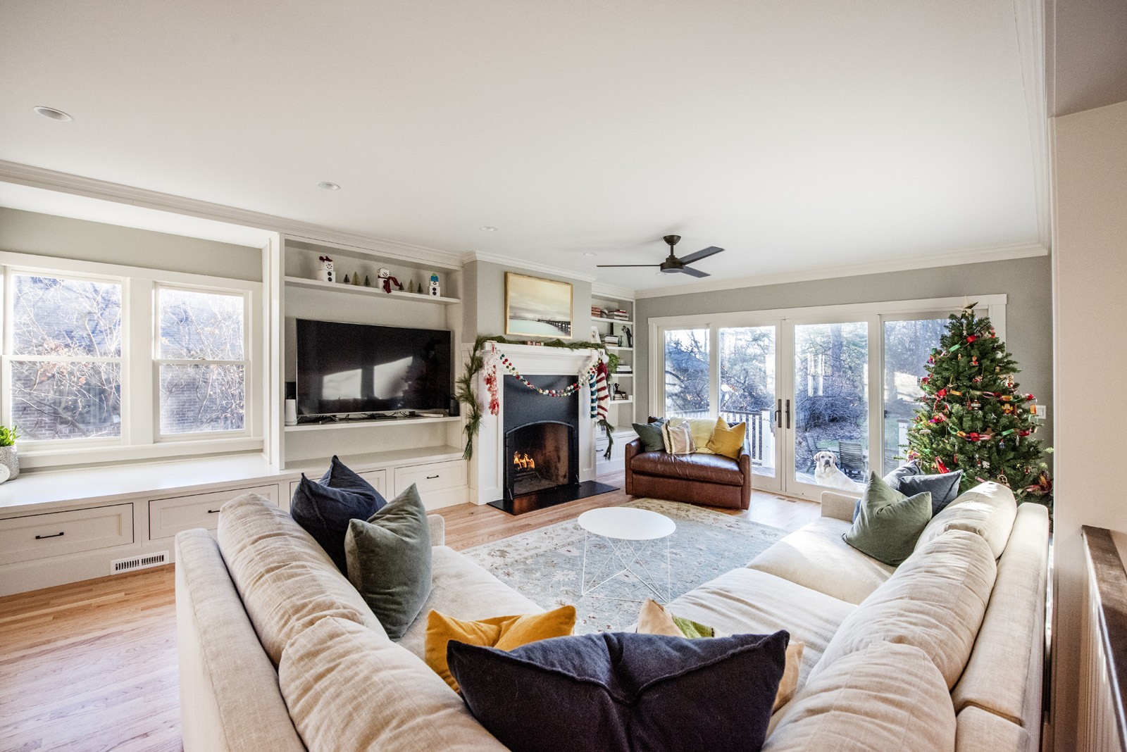 Living room with sectional couch, TV, fireplace, glass doors to outside deck, holiday decorations