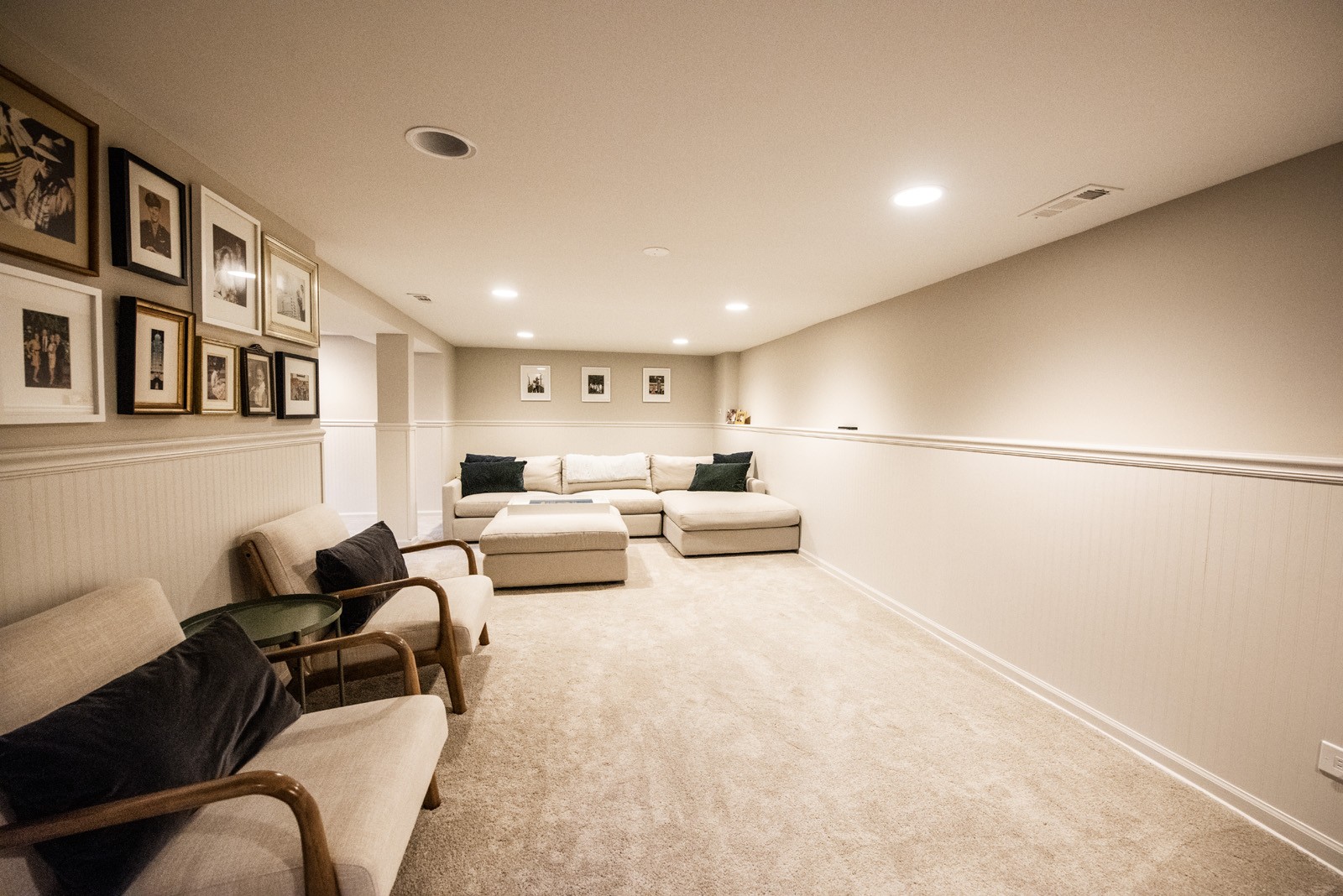 Updated living space with picture wall, white wainscoting, & off-white cloth sectional with matching ottoman & chairs