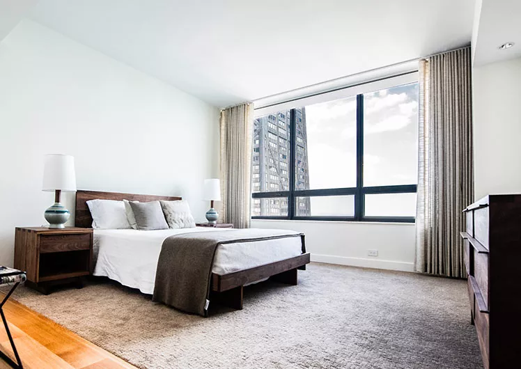 bedroom with white walls tall windows grey curtains and rug wooden bed and nightstands center wall