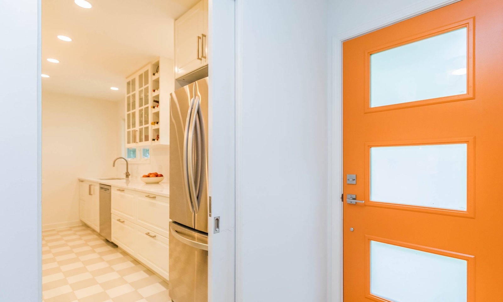 mid century modern ranch renovation and remodel view of entry with orange front door and white kitchen beyond