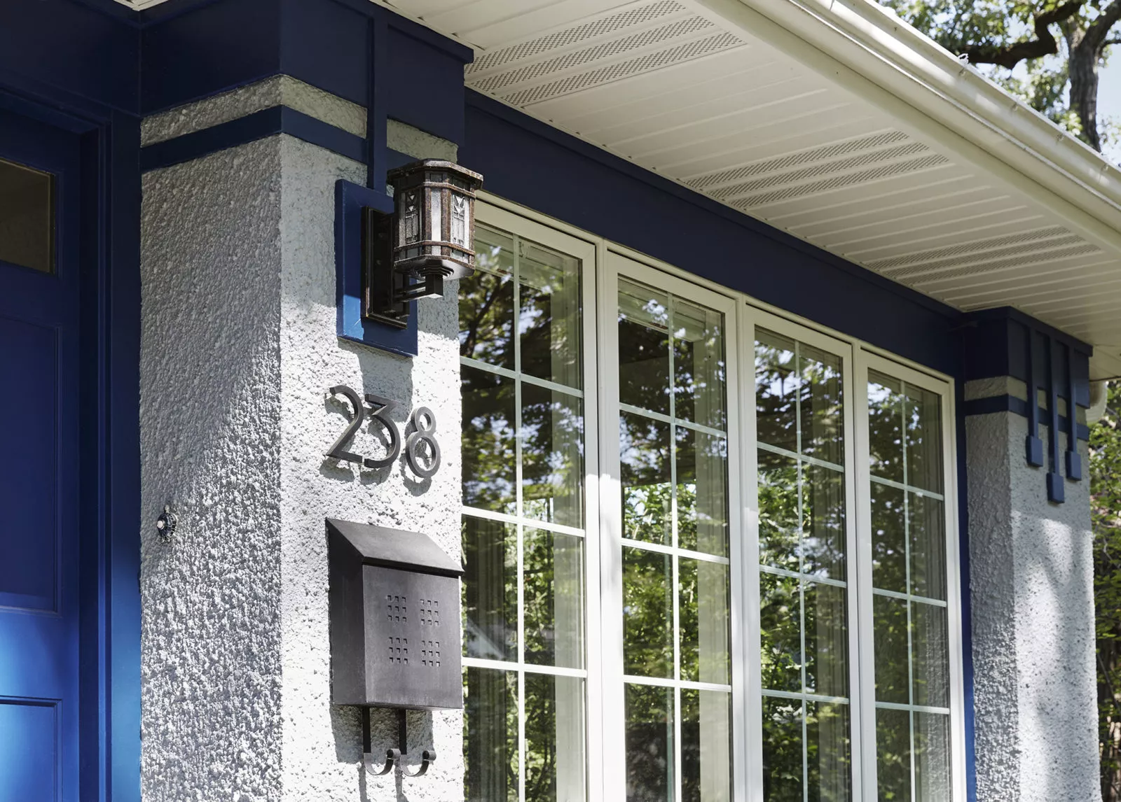 exterior view of front of grey stucco home with blue accents and door house number 238 above mailbox