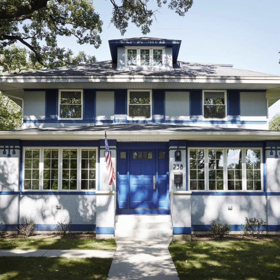 two story grey home with blue front door shutters and accents with american flag hunt next to door