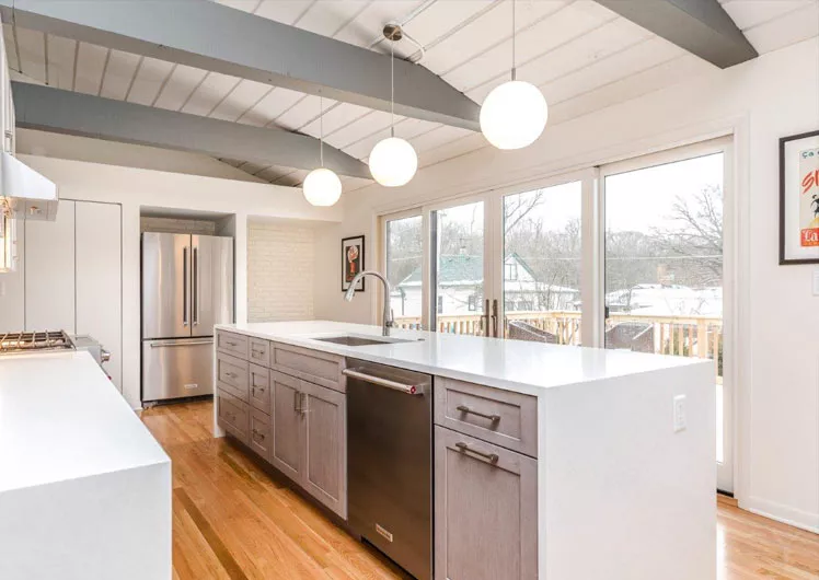 A bright kitchen with a large waterfall island hardwood floors grey ceiling beams and tall doors