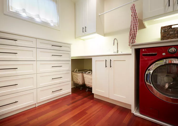 mudroom with white cabinets and 2 drawer sets on hardwood floors and sink next to red clothes washer