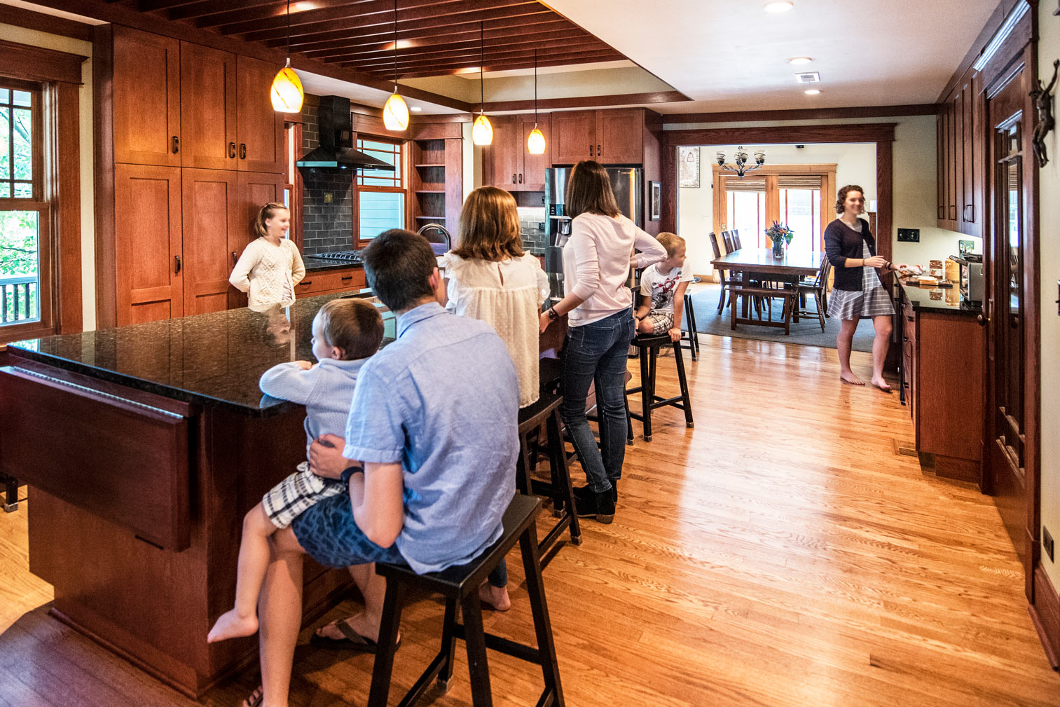 Family in a kitchen with large bar, brown wood cabinets & drawers, adjacent to carpeted dining room