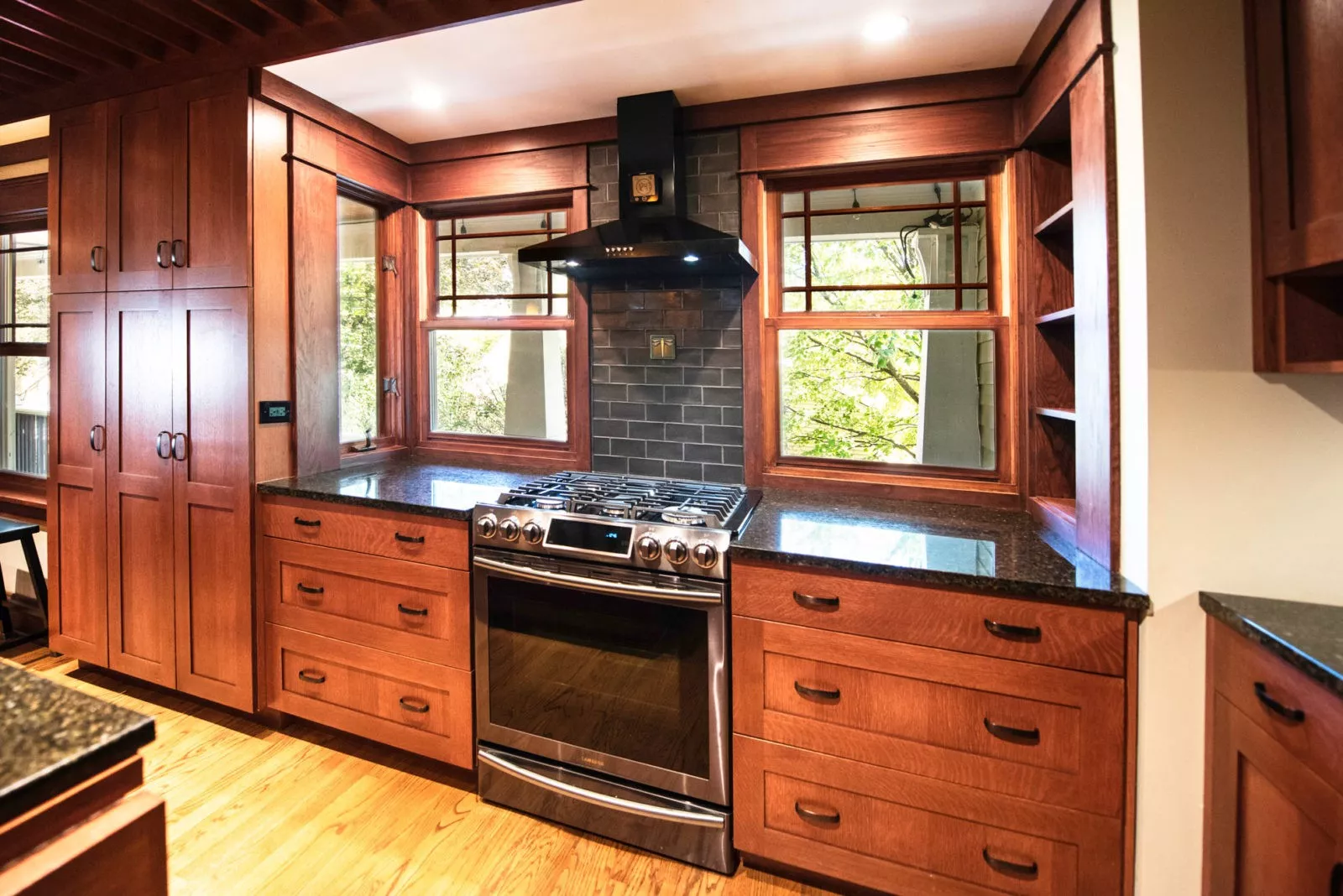 kitchen with dark wooden cabinets black countertops and black hooded vent over stainless steel stove