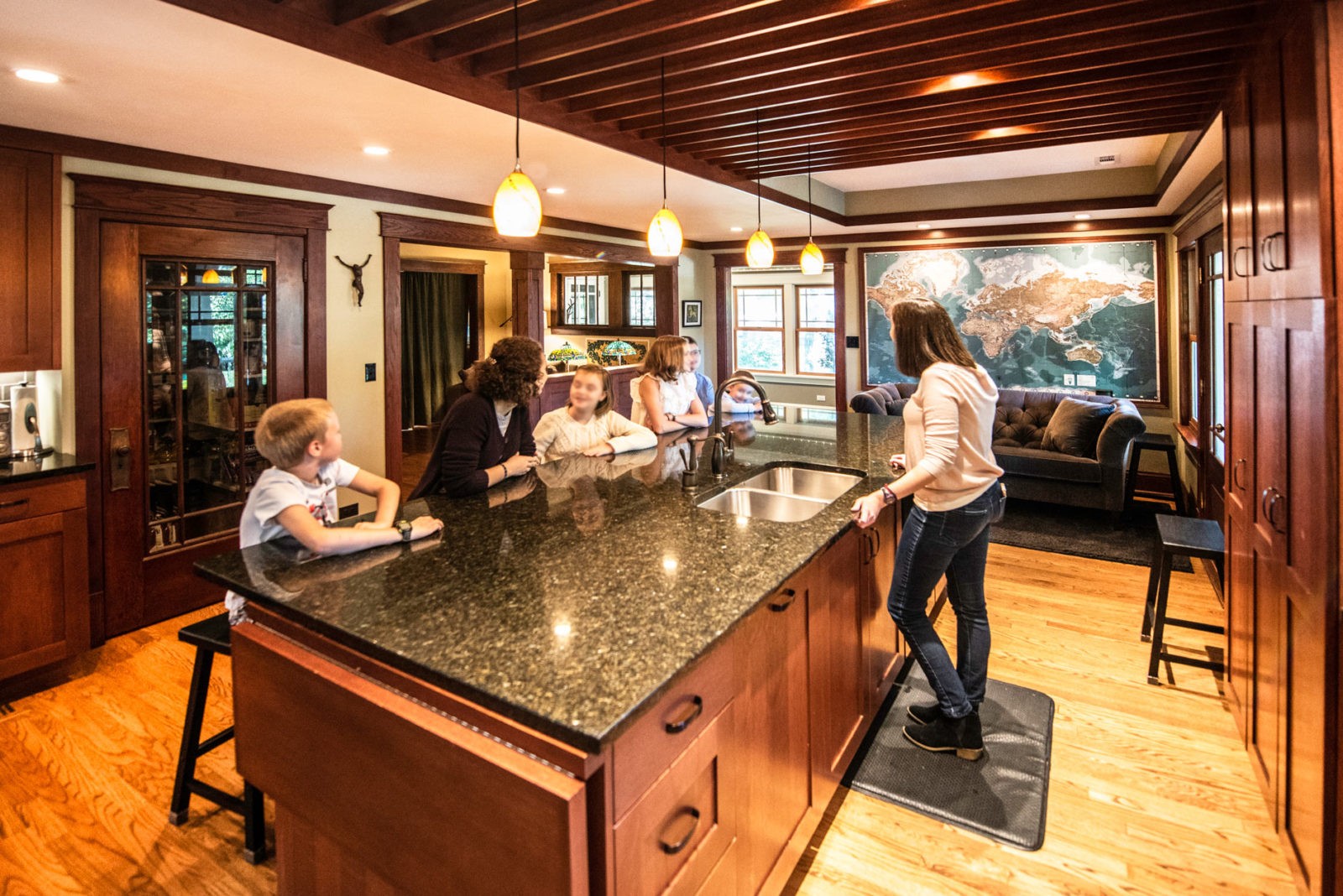 Family in a kitchen with large bar, brown wood cabinets & drawers, couch at far end of room