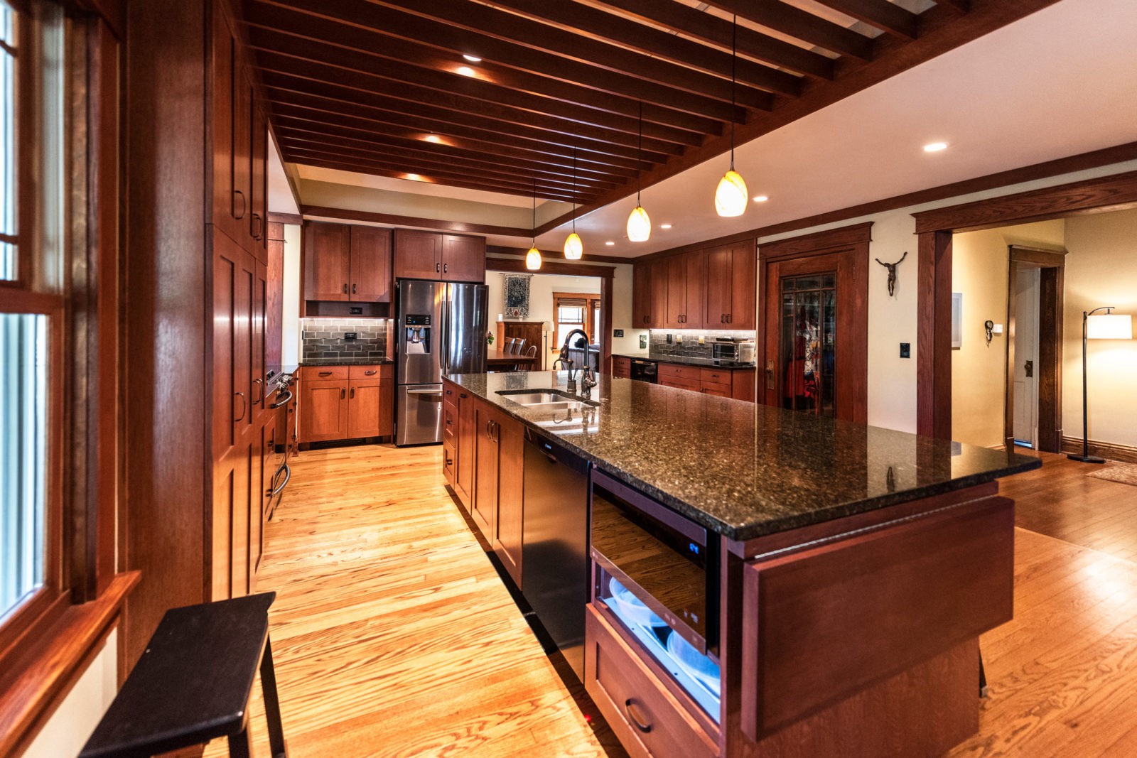 Updated kitchen with dark cherry wood, black marble-topped island, & wood-beamed ceiling