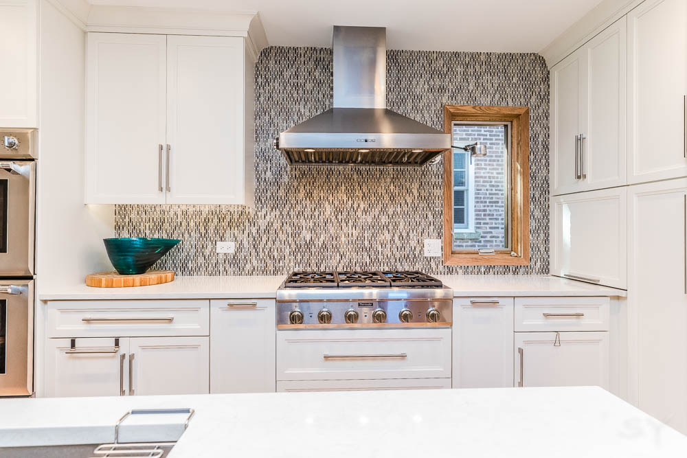 stainless steel hooded vent patterned tile backsplash white cabinets small window in kitchen