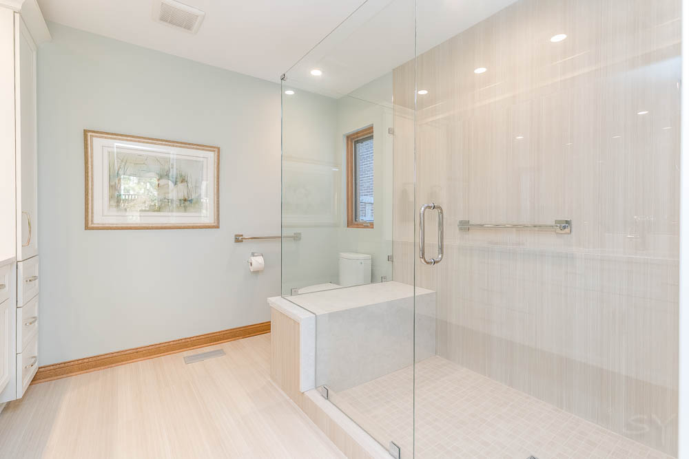 Light-colored bathroom with toilet, large shower with glass walls and grey tile floor