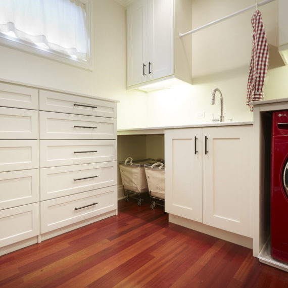 laundry room white wall cabinets and floor drawer unit with black handles and hardwood floors