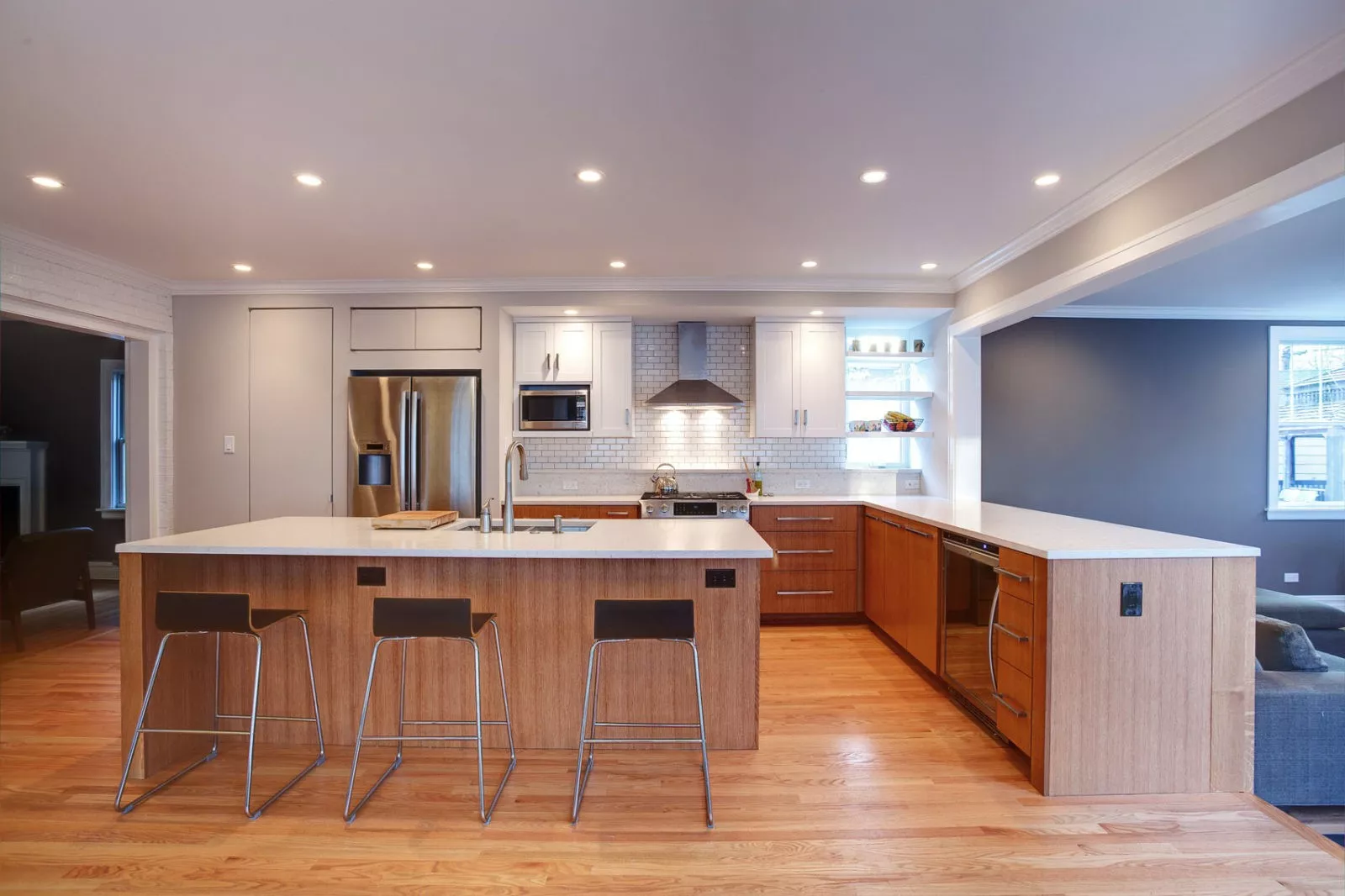 Kitchen with island & stools, brown drawers & white cabinets, connected to living room & den