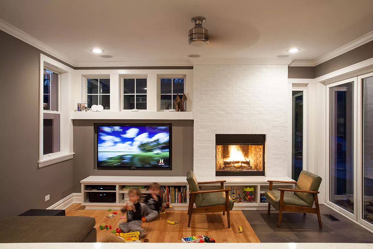 Children playing in newly renovated living room with TV, books, fireplace, midcentury modern furniture.