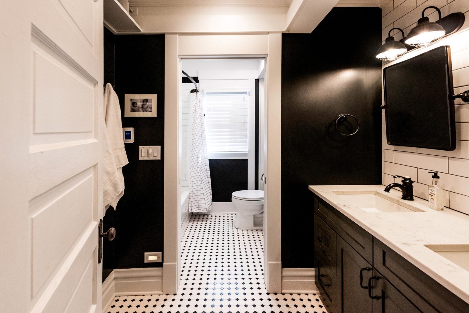 Bathroom with black walls & white trim, toilet, shower, white sinks with mirrors, window, tile floor