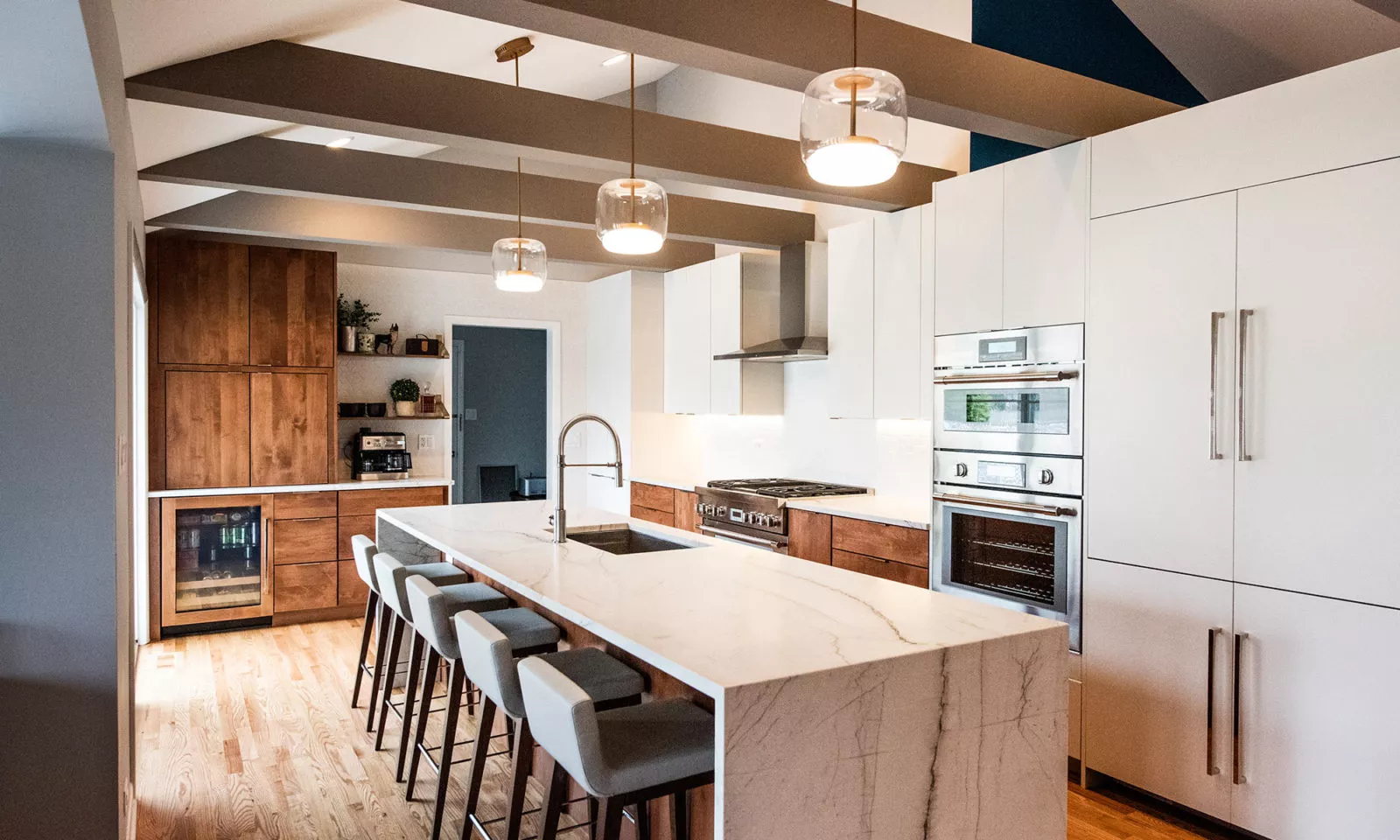 Kitchen with marble island & stools, wood drawers & wine cooler, white cabinets, silver appliances