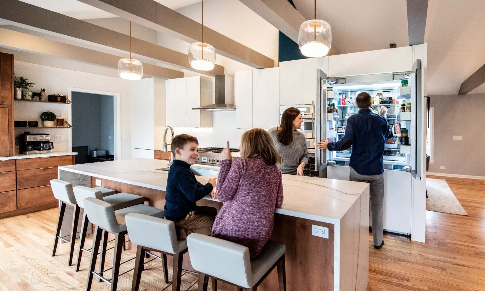 family of 4 in kitchen with large waterfall countertop island white cabinets glass pendant lighting