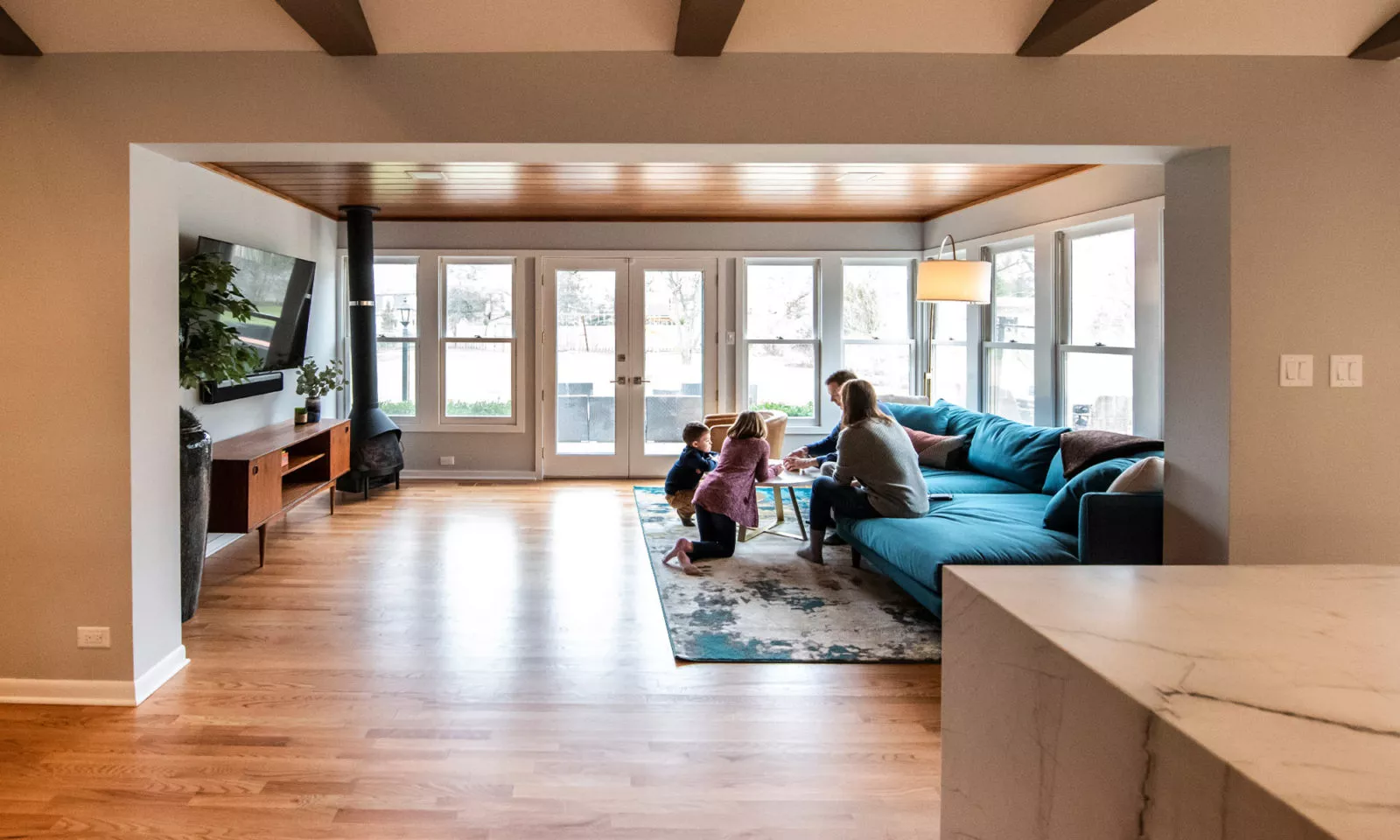 family in livco living room renovation on hardwood flooring white framed windows cast iron heater