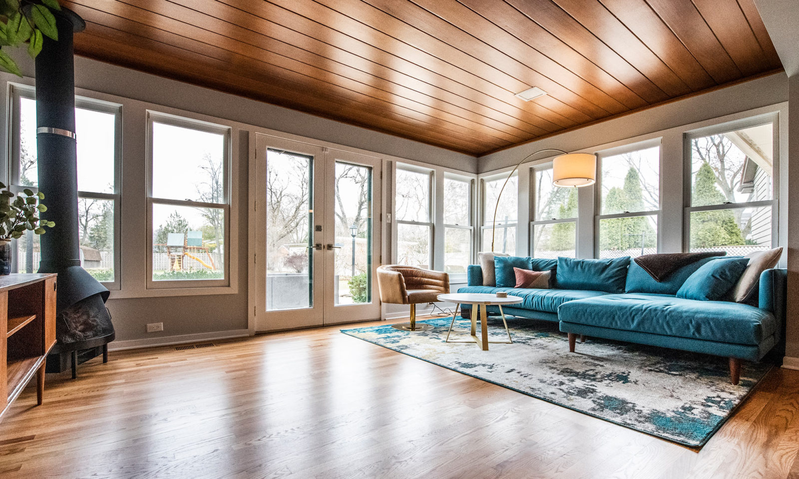 Bright living room with hardwood floors and ceiling a blue sectional and cast iron fireplace