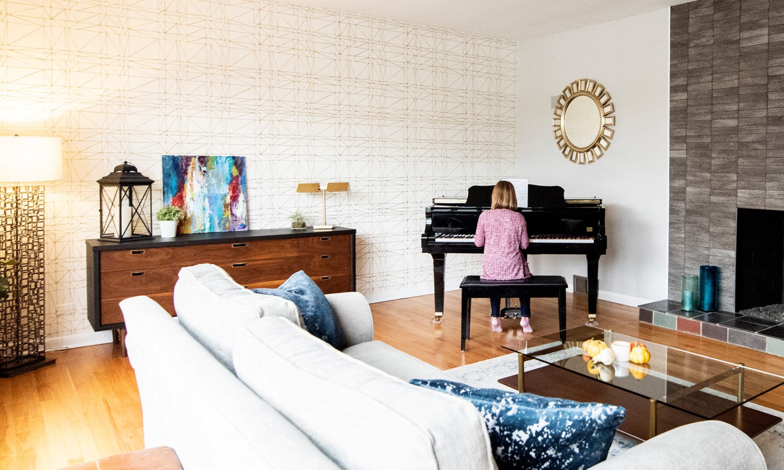 Living room with couch, fireplace, cabinet, and girl sitting at a piano in the corner