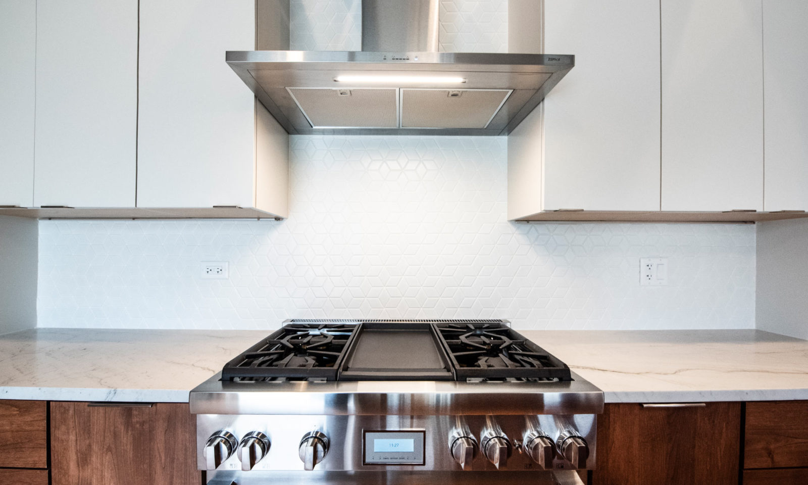 stainless steel range and hooded vent between white cabinets marble countertops brown lower cabinets
