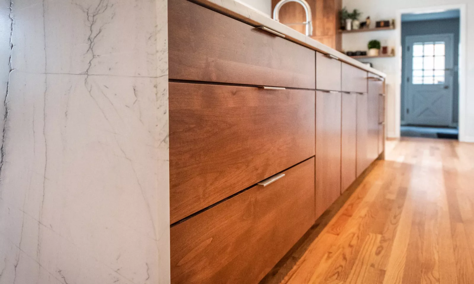 LivCo kitchen remodel brown lower cabinetry with soft close surrounded by marble waterfall island