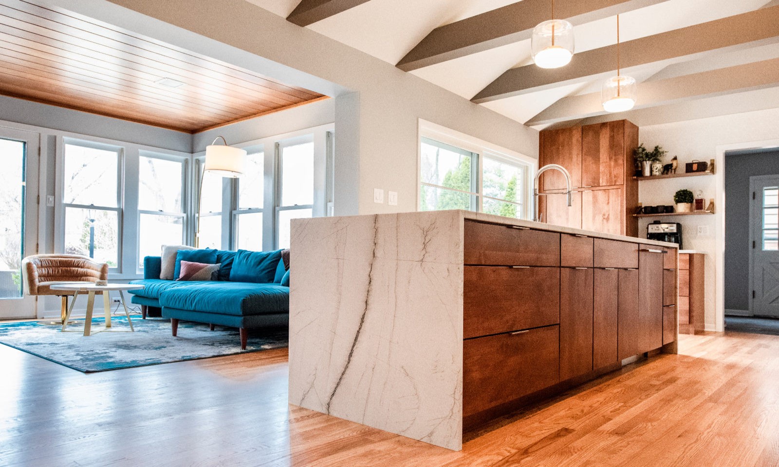 white waterfall island deep brown cabinets & hardwood floors in front of sunroom with blue sectional