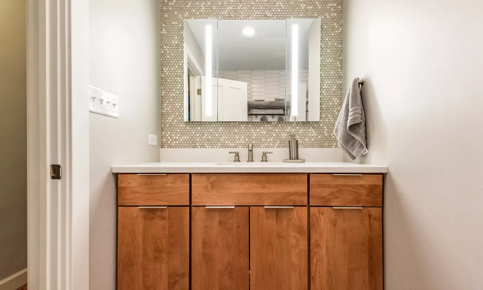 cherry vanity with penny tile backsplash and lighted mirror