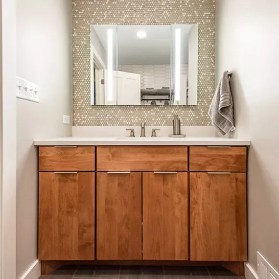 cherry vanity with penny tile backsplash and lighted mirror in recentky remodeled bathroom