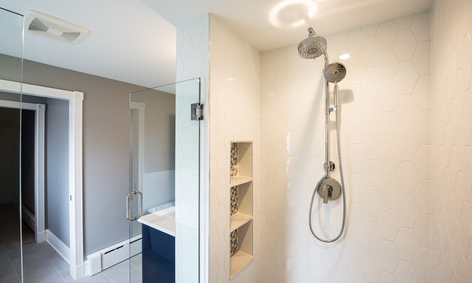Newly renovated standing shower with white hexagonal tiles on the walls and silver fixtures
