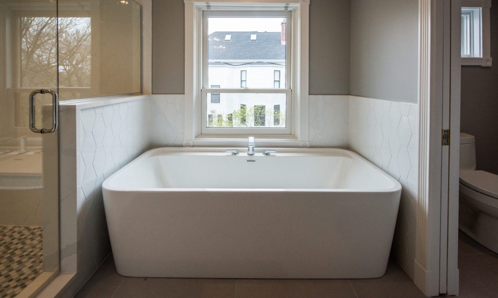 Newly renovated large white tub under a window in a white bathroom