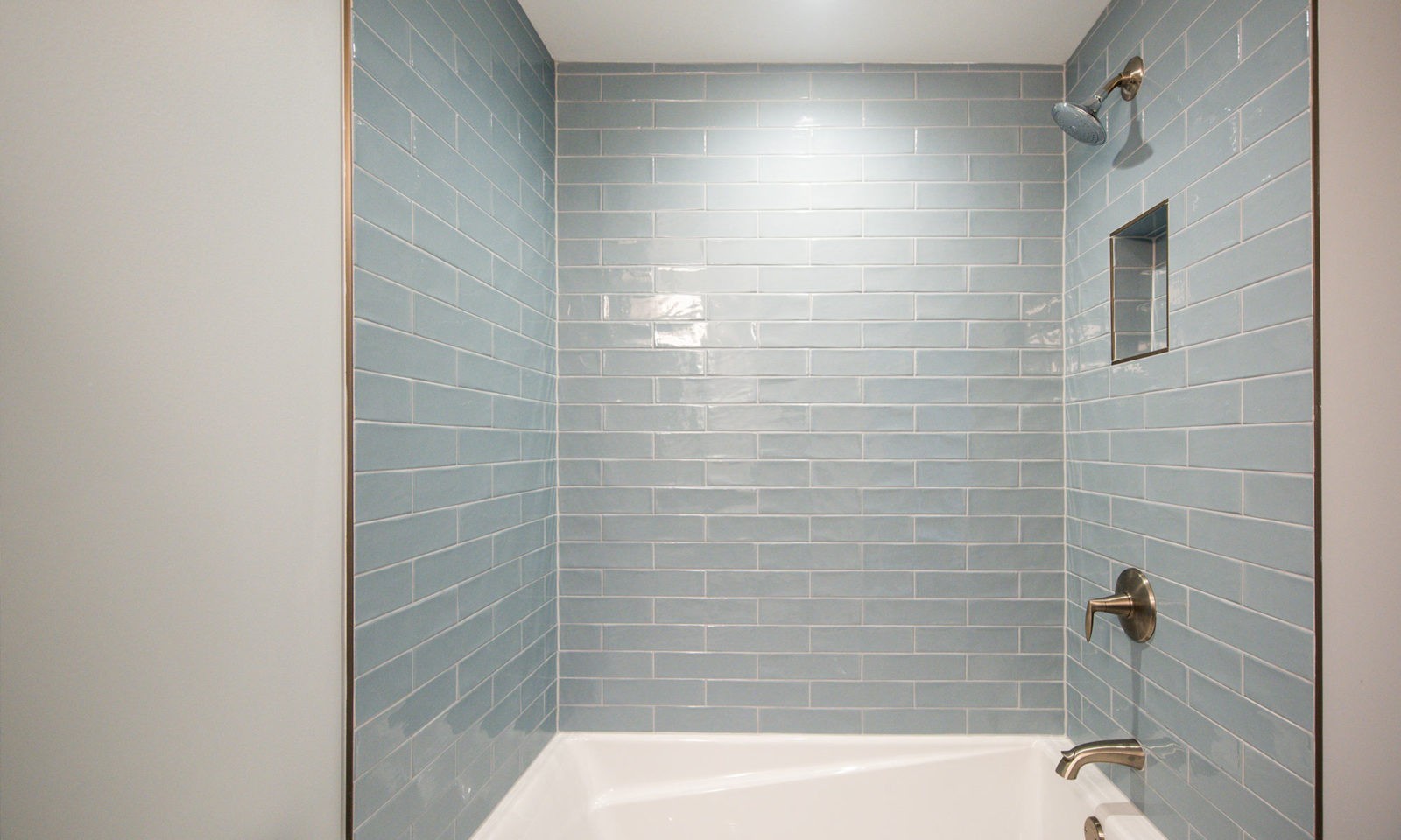 Newly renovated shower with blue-gray tiles on the wall and silver fixtures