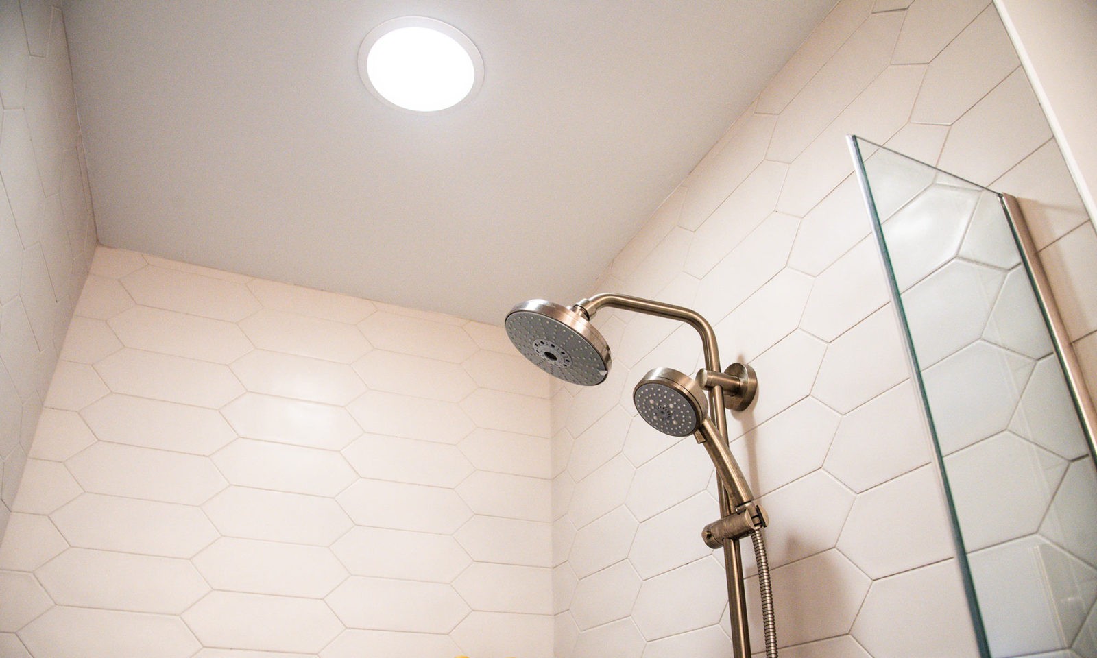 Newly renovated white tile standing shower with silver fixtures and recessed lighting