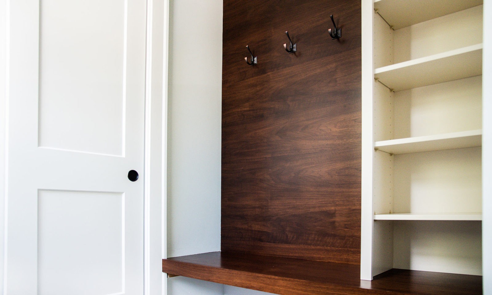 Newly renovated organizing space with hooks on wooden wall and cream colored shelves